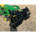 Black steel grapple attachment mounted on green compact tractor on dry grass outdoors