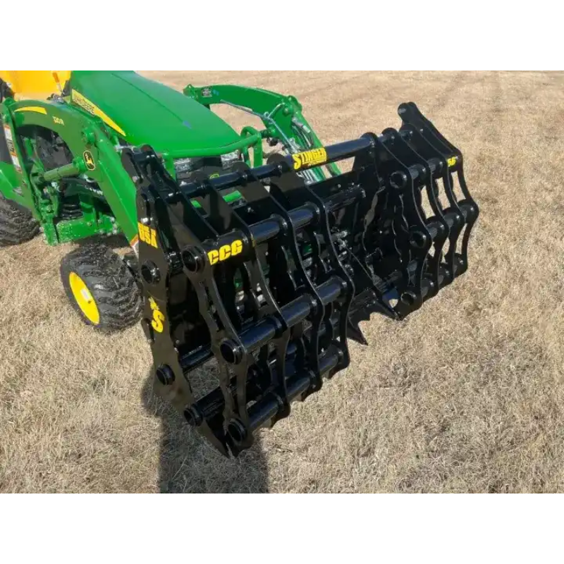 Black steel grapple attachment mounted on green compact tractor on dry grass outdoors