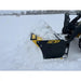 Yellow and black skid steer snow pusher attachment angled left, pushing snow on flat, open snow-covered field outdoors