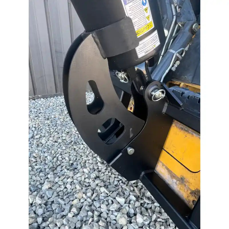 Close-up of black metal hinge bracket connecting loader arm to concrete mixer attachment over gravel ground