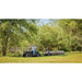 Man driving ATV pulling Swisher log skidder with large timber across grassy field, gallery position 1