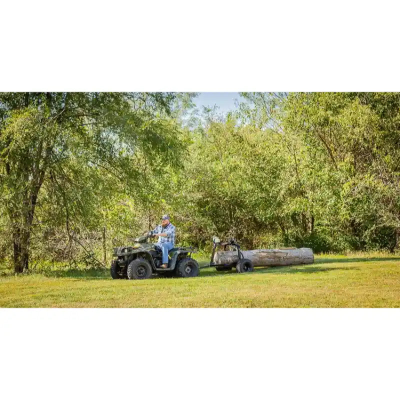 Man driving ATV pulling Swisher log skidder with large timber across grassy field, gallery position 1