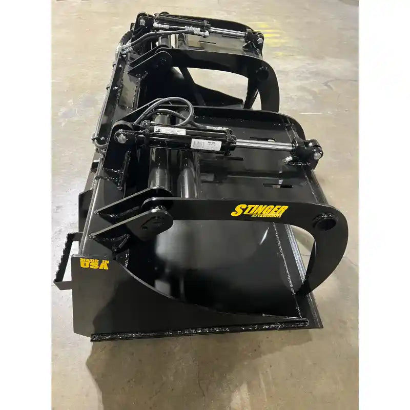 Black steel grapple bucket attachment with hydraulic clamp arms and cylinders on concrete floor indoors