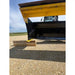 Close-up of steel skid steer snow pusher blade edge with yellow wear guard resting on gravel surface outdoors