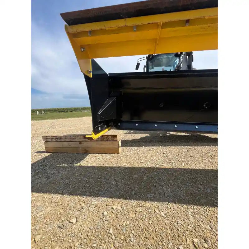 Close-up of steel skid steer snow pusher blade edge with yellow wear guard resting on gravel surface outdoors