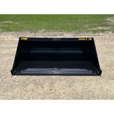 Front view of black skid steer material bucket with smooth interior and yellow Series 3 78 decals on gravel surface