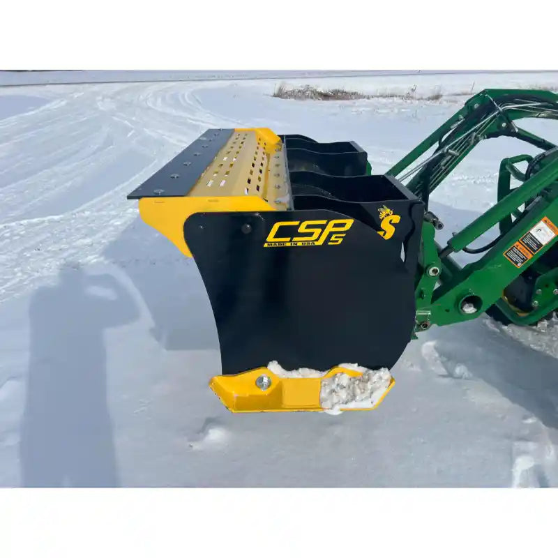 Black and yellow steel snow pusher attachment connected to green loader arm with snow on cutting edge on snowy ground