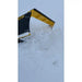 Yellow and black skid steer snow pusher attachment raised, pushing a large pile of snow outdoors on cloudy day