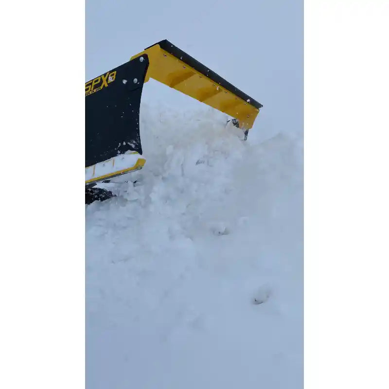 Yellow and black skid steer snow pusher attachment lifting and throwing a large mass of snow outdoors