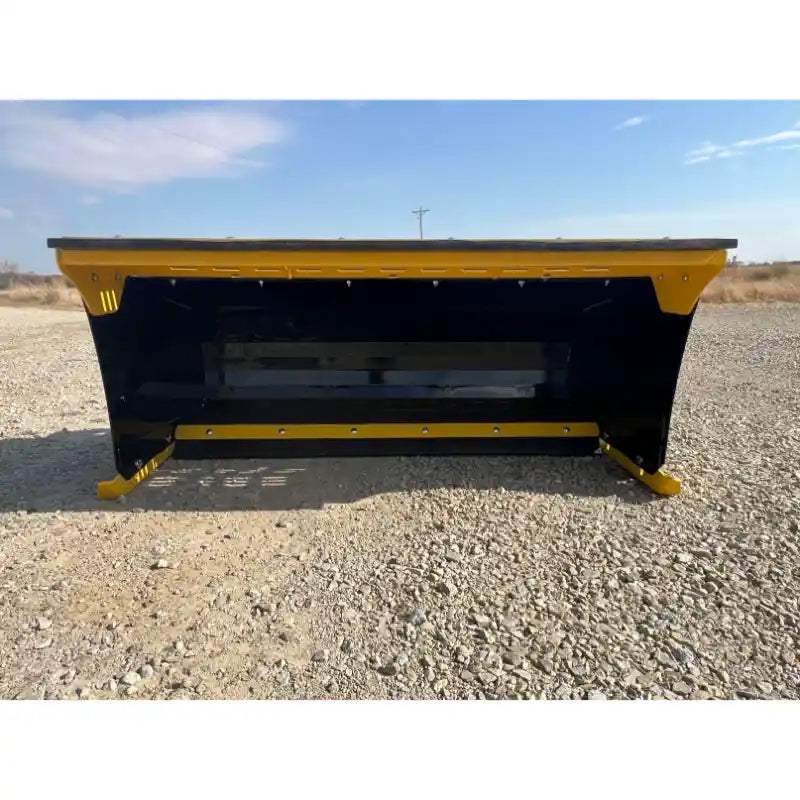Front view of yellow and black skid steer snow pusher attachment resting on gravel surface outdoors