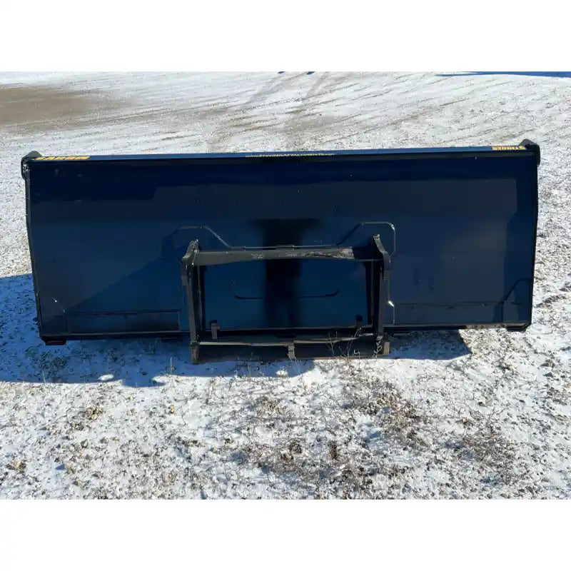 Rear view of black steel skid steer high-volume bucket attachment resting on gravel and light snow ground
