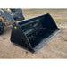 Angled front view of black steel skid steer bucket attachment resting on dirt surface at outdoor site