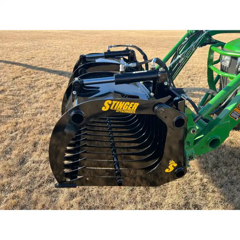 Black steel grapple attachment with hydraulic cylinders and closely spaced curved tines on compact green loader arm