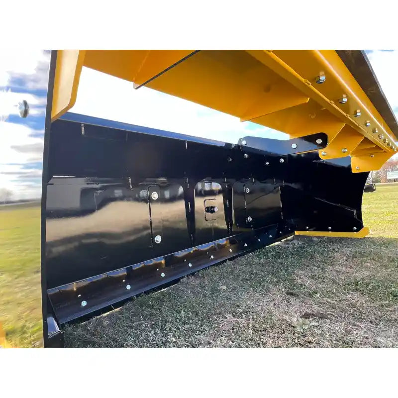 Underside view of black steel snow pusher blade with reinforced edge and yellow mounting framework on grass field