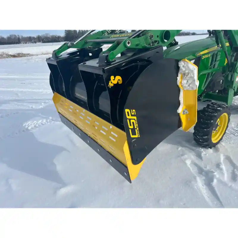 Black and yellow steel snow pusher attachment tipped down, mounted on green compact tractor on snowy field