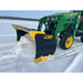 Yellow and black steel snow plow attachment clearing snow mounted on green tractor with visible tire tracks in snow