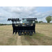 Front view of black skid steer grapple attachment with open tines on grass field under cloudy sky