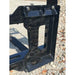 Close-up of black steel skid steer pallet fork mounting bracket with rectangular cutout on gravel surface outdoors