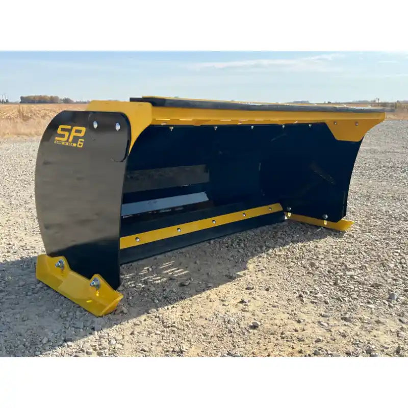 Wide black and yellow skid steer snow pusher attachment with reinforced cutting edge on gravel surface