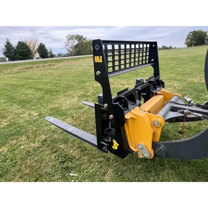 Black steel skid steer pallet fork attachment with perforated backrest and two flat fork tines on grass field