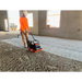 Construction worker in orange shirt and beige pants operating orange and black MBW plate compactor on gravel floor inside building