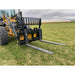 Yellow skid steer loader with black pallet fork attachment featuring two flat steel tines on grass field