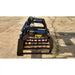 Black metal grapple skid steer attachment with horizontal tubular tines and hydraulic cylinders on concrete surface outdoors