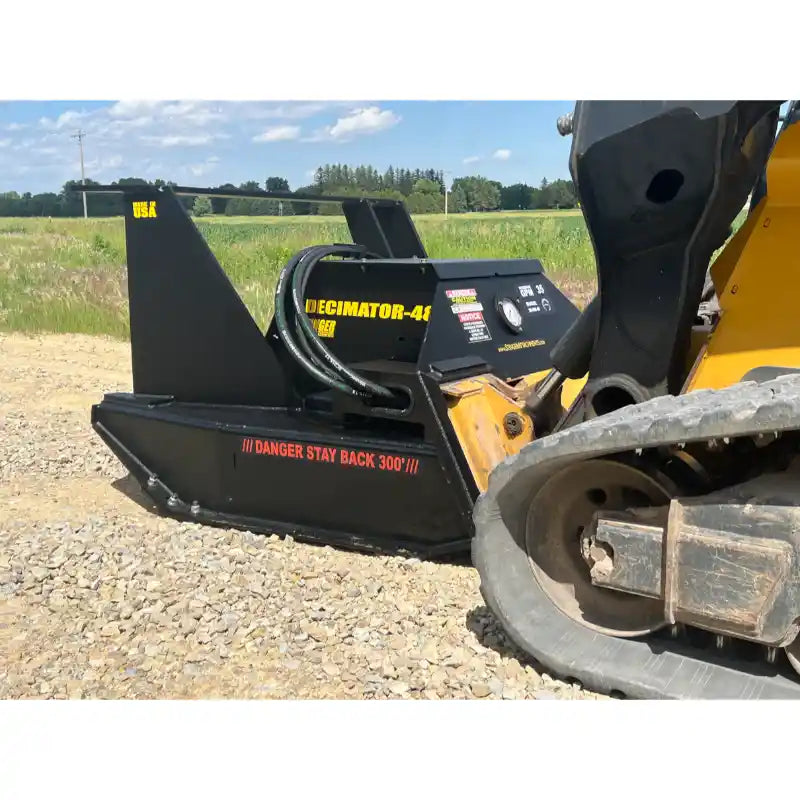 Black skid steer attachment with hydraulic hoses on gravel surface under clear sky