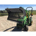 Green compact loader with a rock bucket attachment featuring closely spaced curved tines lifted above gravel ground