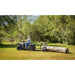 Side view of rider operating Swisher ATV Log Skidder towing large log across grassy clearing, gallery position 1