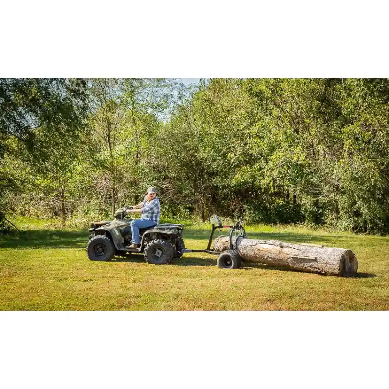 Side view of rider operating Swisher ATV Log Skidder towing large log across grassy clearing, gallery position 1