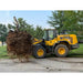 Yellow Komatsu WA270 loader lifting large tree root ball on grassy and gravel surface near trees