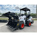 White skid steer with black multi-tine grapple attachment and orange wheels parked on asphalt near fence under cloudy sky