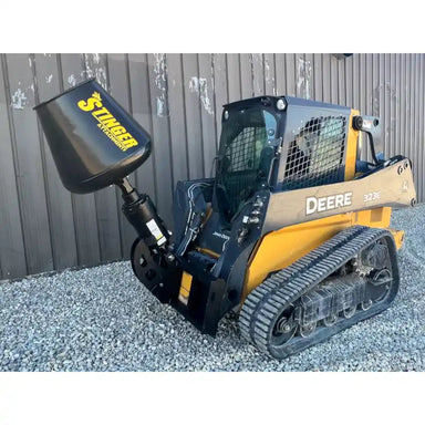 Yellow John Deere compact track loader with black Stinger concrete mixer attachment on gravel surface near metal building wall