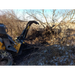 Yellow skid steer with black curved stump grapple attachment holding uprooted tree and branches on dirt terrain