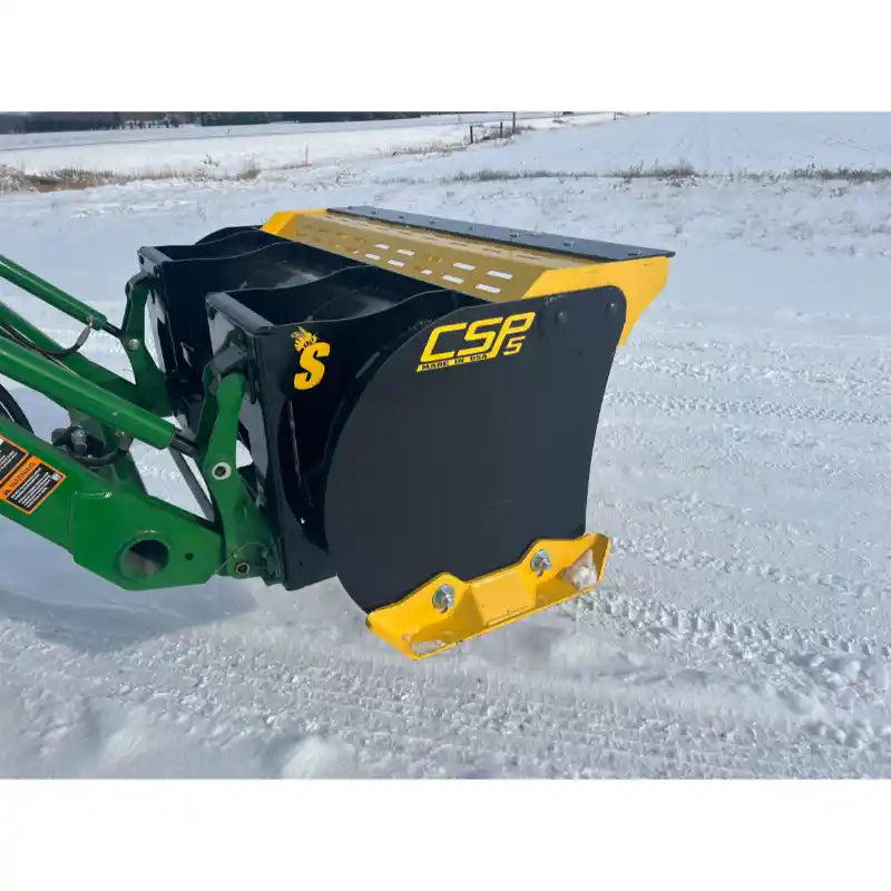 Compact black and yellow snow pusher attachment mounted on green skid steer loader arm in snowy field