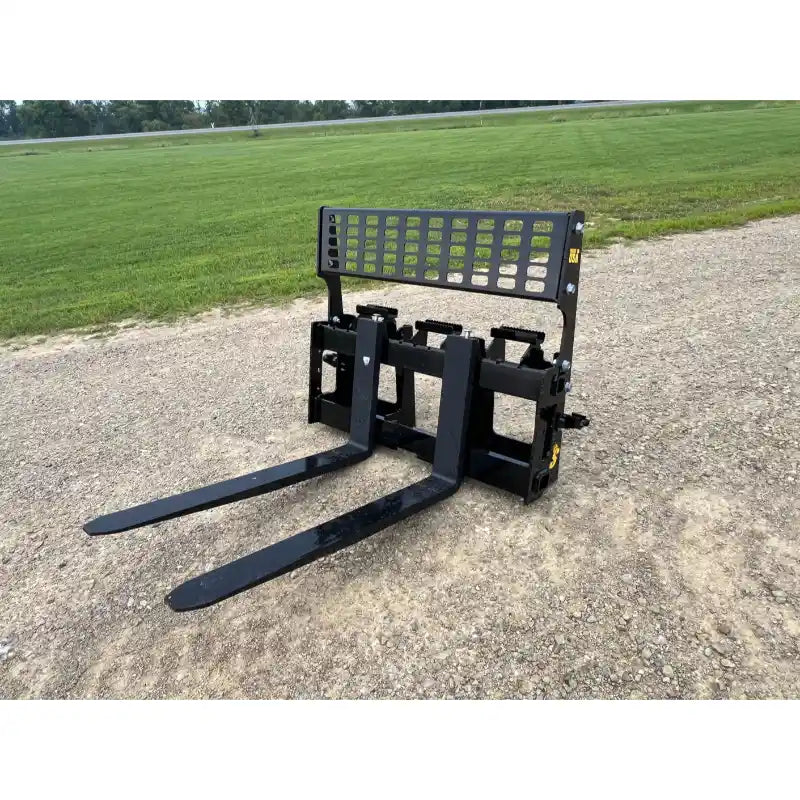 Black steel skid steer pallet fork attachment with perforated mesh backrest and two long flat tines on gravel surface