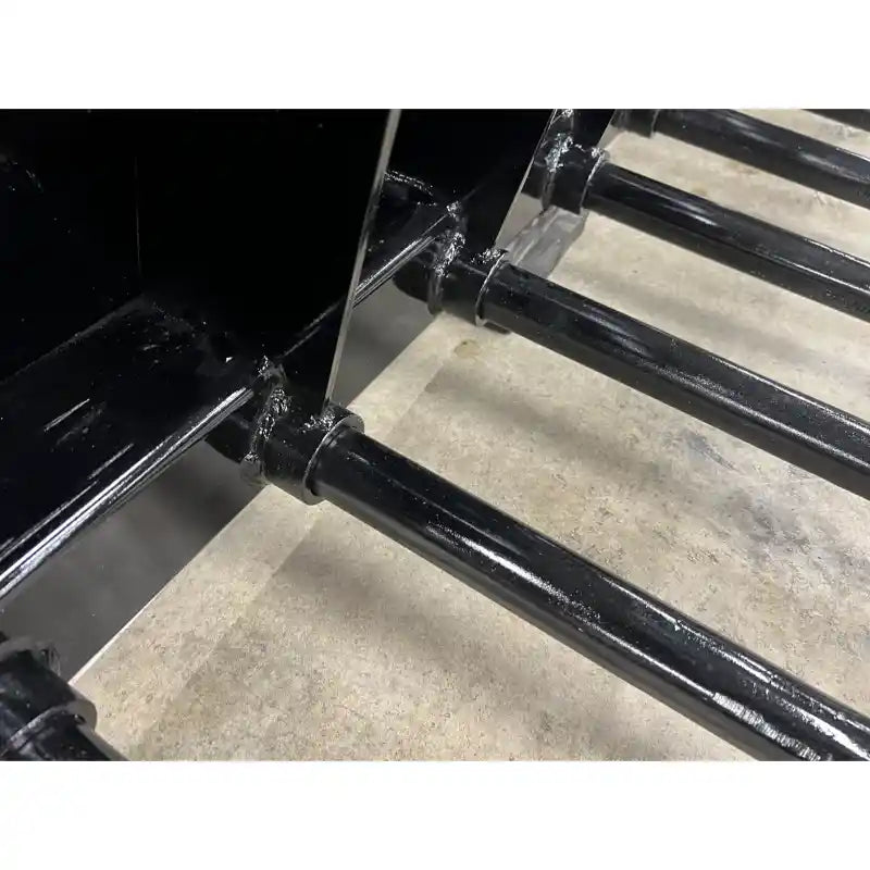 Close-up of black metal manure spear tines with round weld joints and welded mounting plate on concrete floor indoors