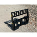 Black steel skid steer pallet fork mounting frame with open grid backrest on gravel surface near stone pile