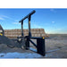 Black steel bale spear skid steer attachment with dual vertical support bars and dual horizontal tines in outdoor dirt setting