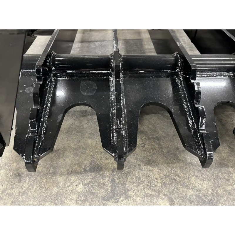 Close-up of black steel skid steer grapple attachment teeth with welded reinforcements on concrete floor
