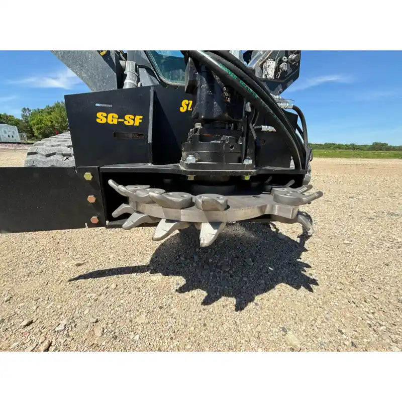 Skid steer stump grinder attachment with steel cutting wheel, multiple teeth, hydraulic motor, and black mounting frame on gravel surface