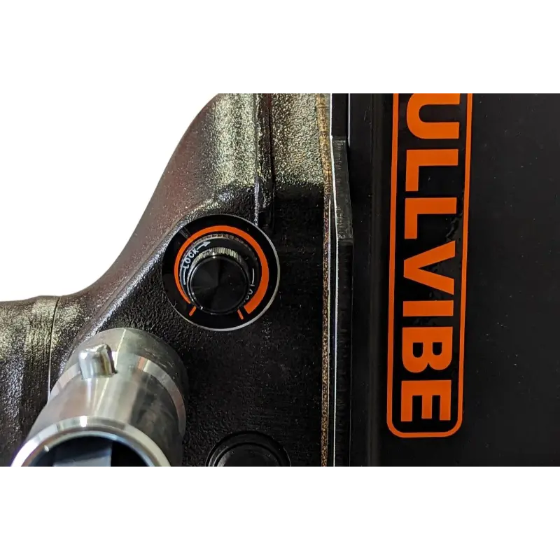 Close-up of black mechanical vibration control knob with orange markings on steel equipment housing near orange BullVibe label