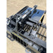 Close-up of black steel skid steer grapple attachment showing hydraulic cylinders, hoses, and welded tine frame on concrete