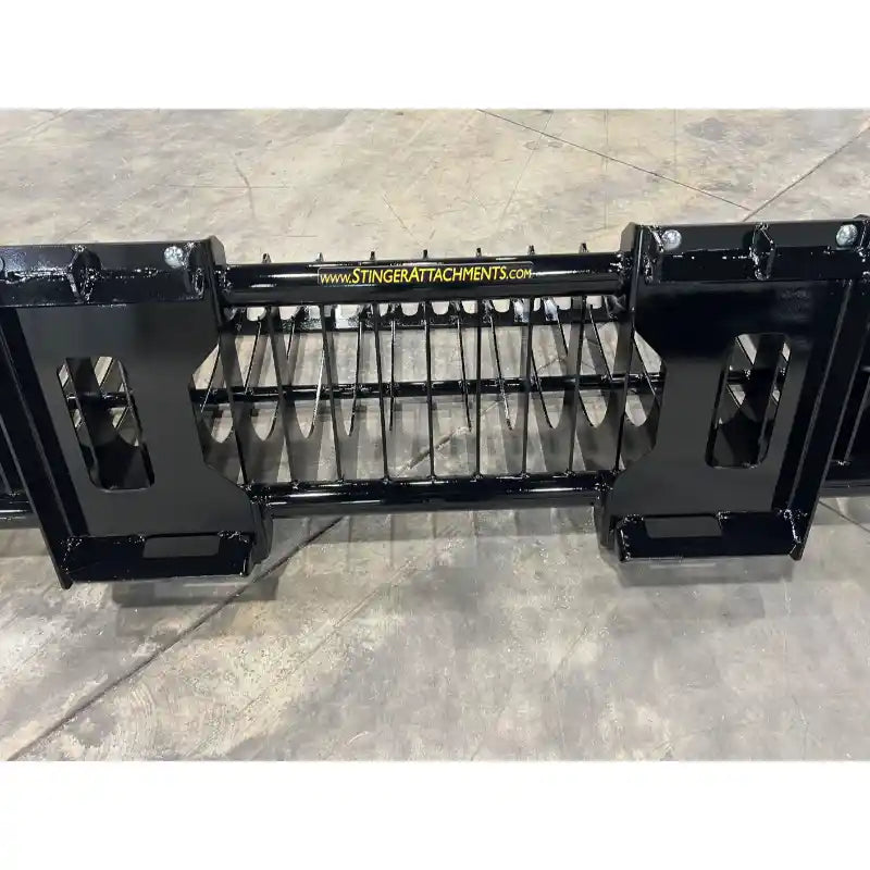 Black skid steer attachment with narrow spaced tines and reinforced mounting frame on concrete floor