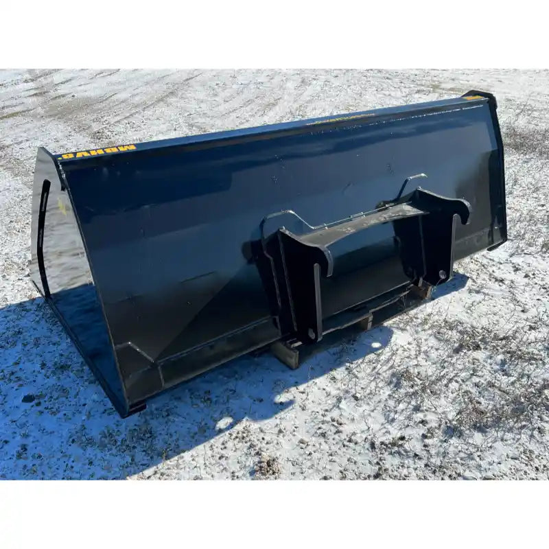 Back-left angled view of black steel skid steer material bucket attachment resting on snowy gravel surface