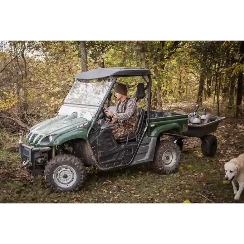 Green utility vehicle towing Swisher 16 cu ft poly cart with gear in wooded area, gallery position 1