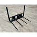 Black metal bale spear skid steer attachment with four pointed tines and two vertical support arms on dirt surface viewed from front right angle