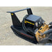 Black steel hydraulic mulcher attachment with hoses and warning labels connected to skid steer loader on gravel surface