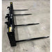 Black steel bale spear attachment with four pointed tines on concrete floor viewed at angled side from right